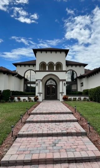 A white stucco mansion with a brick walkway, against a blue sky.