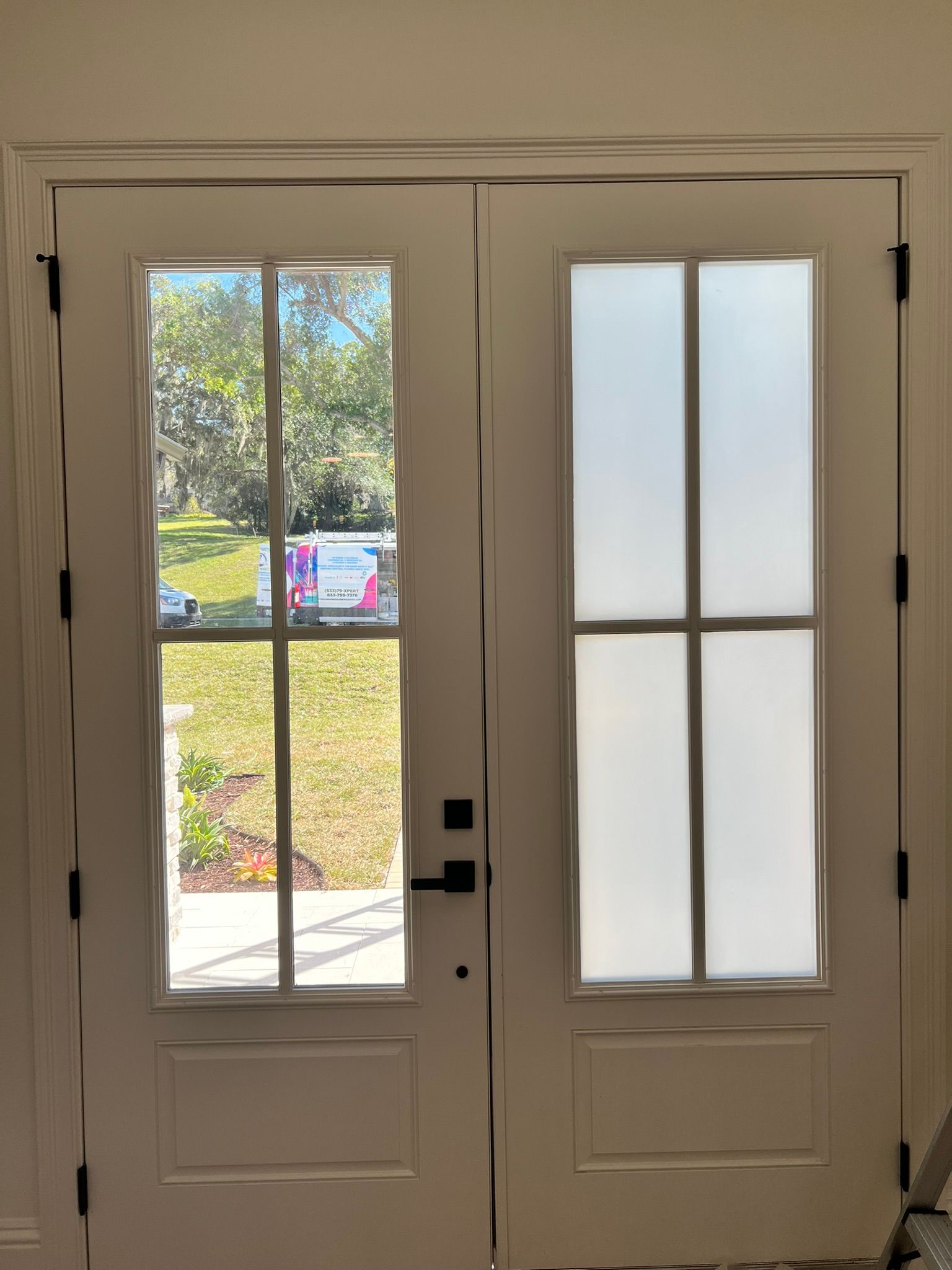 White double doors with a clear window and a frosted window. Black hardware, neutral setting.