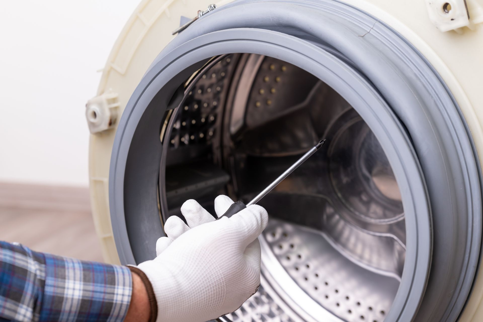 Gloved hand with a screwdriver points to the inside of a washing machine. Gloved hand with a screwdriver points to the inside of a washing machine.