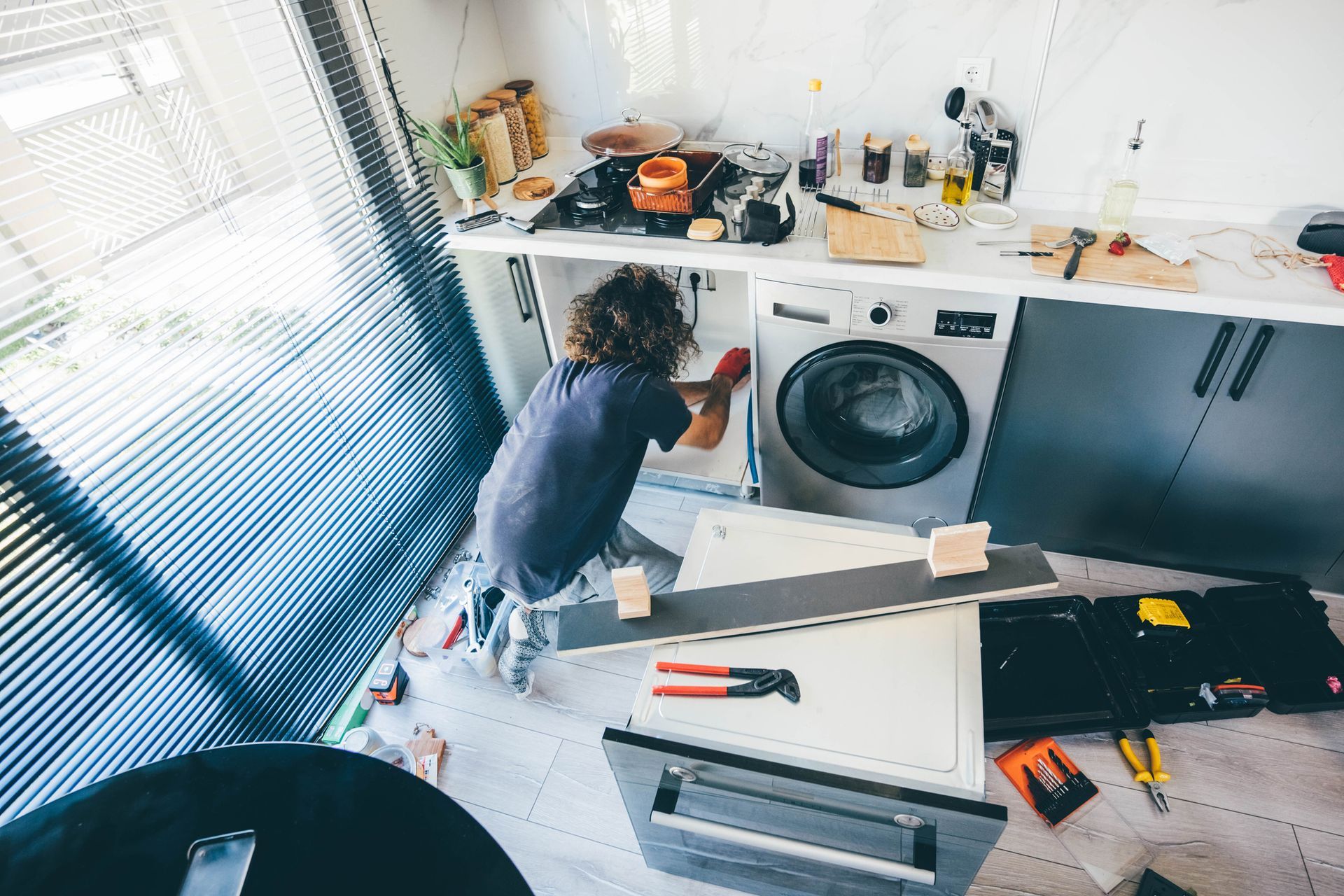 Person working on kitchen cabinets near a washing machine. Tools and materials are on the floor.