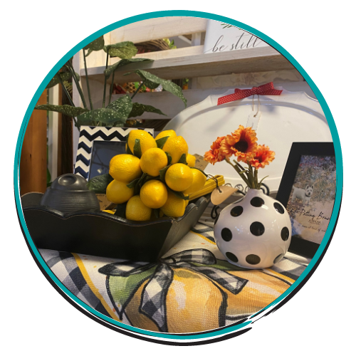 Decorative tabletop display with yellow lemons, black teapot, polka-dot vase, and orange flowers