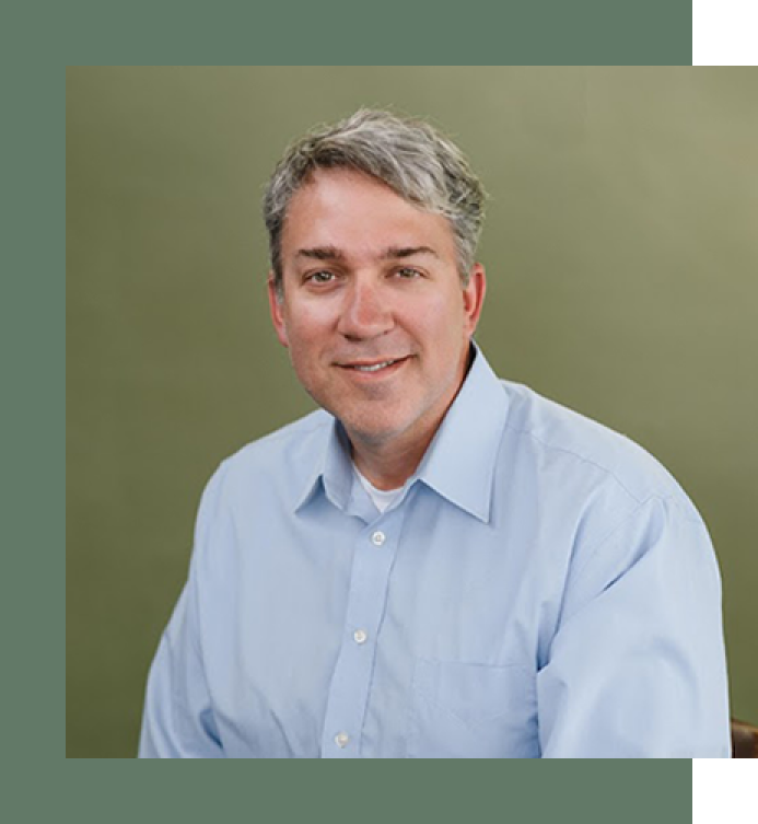 A man in a blue shirt is sitting in front of a green wall.