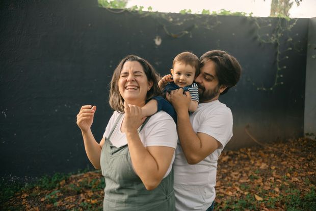 A man and a woman are holding a baby on their shoulders.