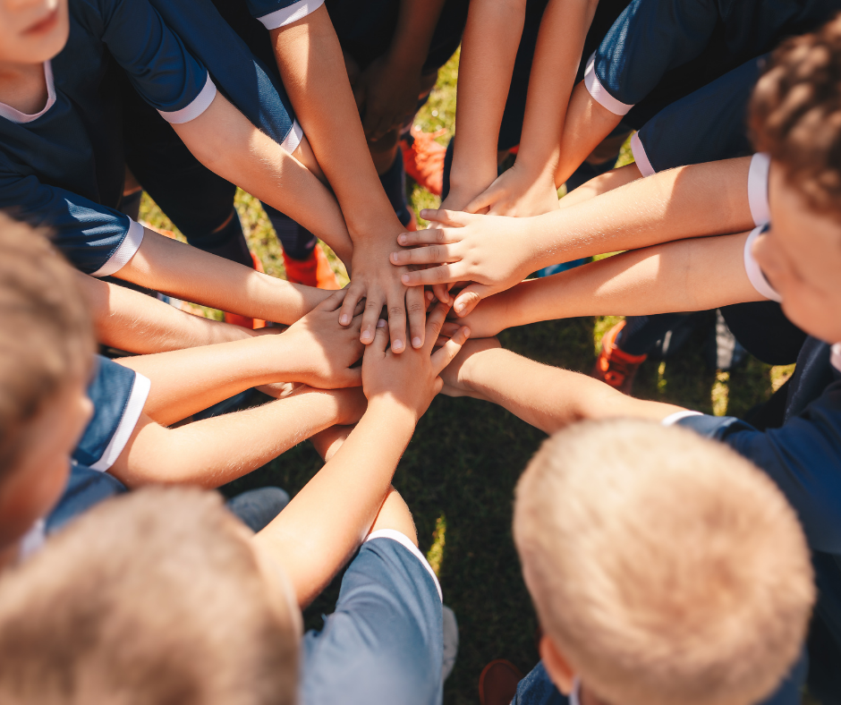Team of young athletes with hands stacked in a huddle, in a green field, wearing blue uniforms.