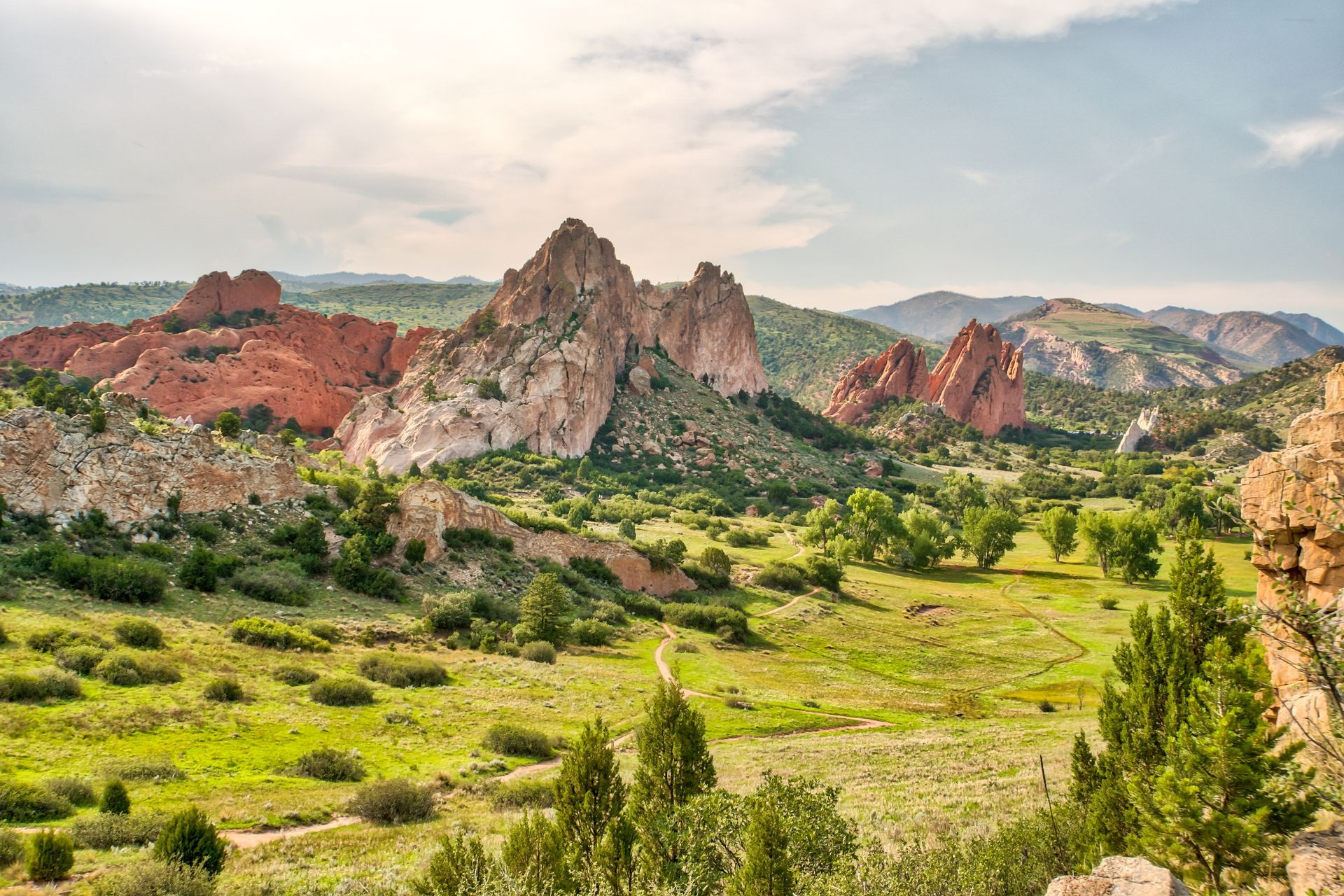 Rocky mountains in Garden of the Gods park, Colorado, with red rock formations, green valleys, and blue sky.