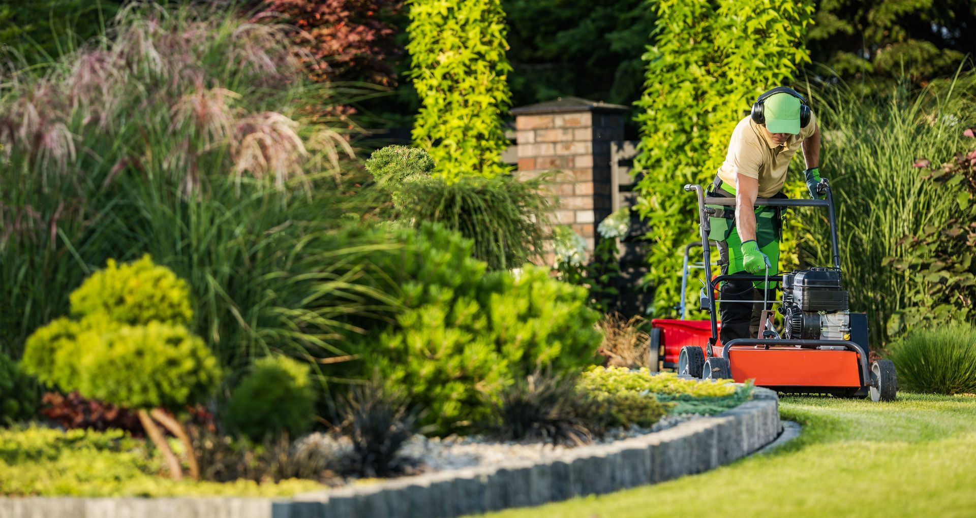 Person mowing a manicured lawn in a landscaped garden, wearing protective gear.