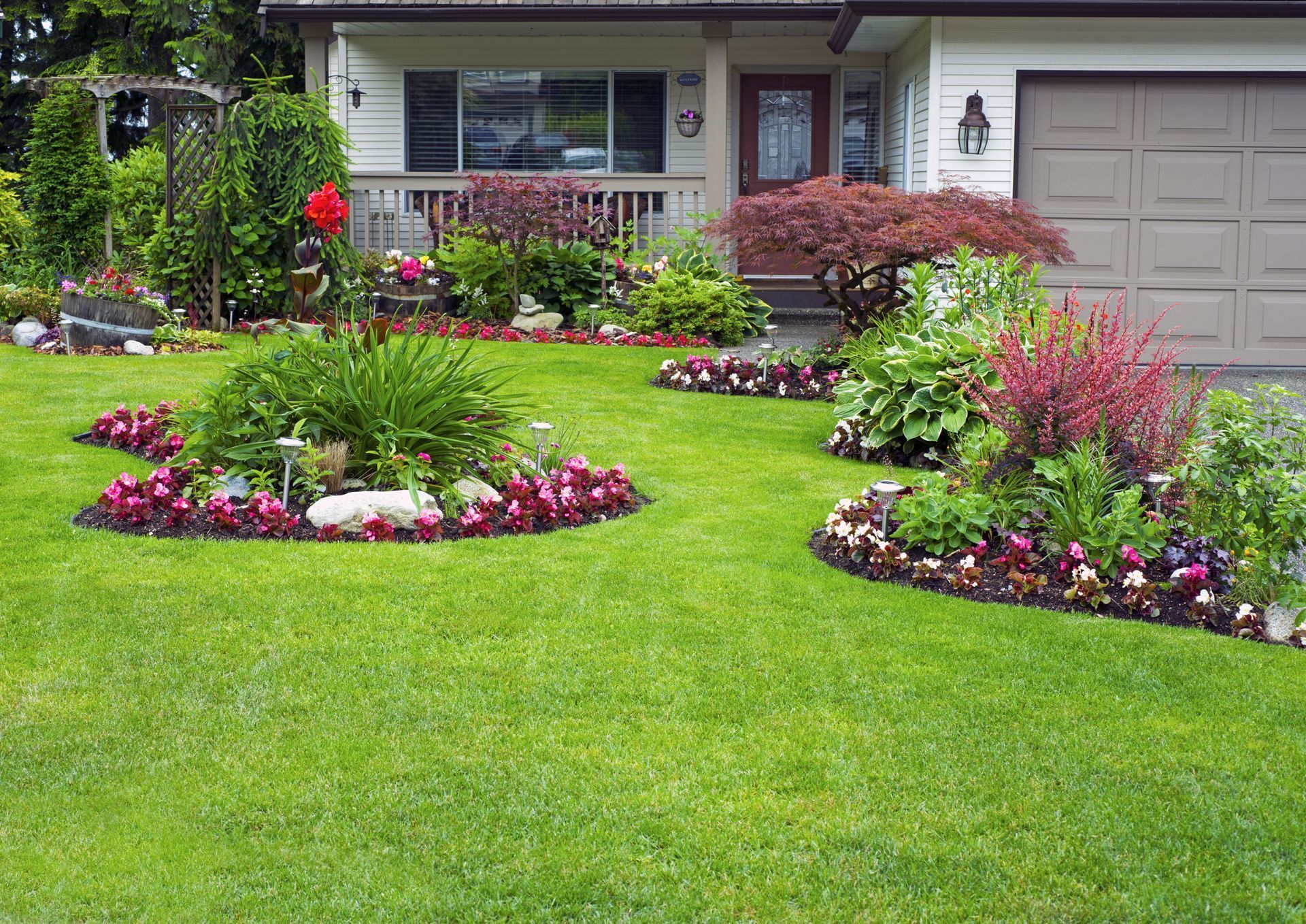 A well-manicured lawn with flower beds in front of a house with a garage.