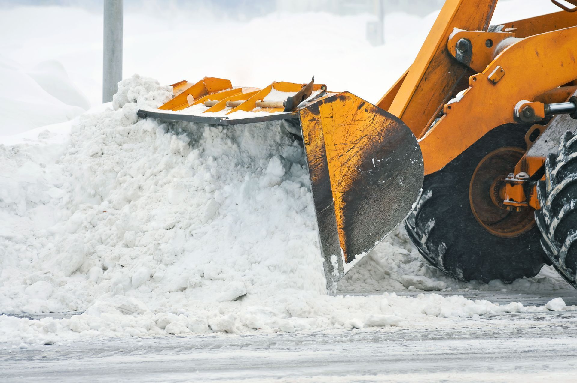 Yellow front-end loader clearing a large pile of snow from a road.