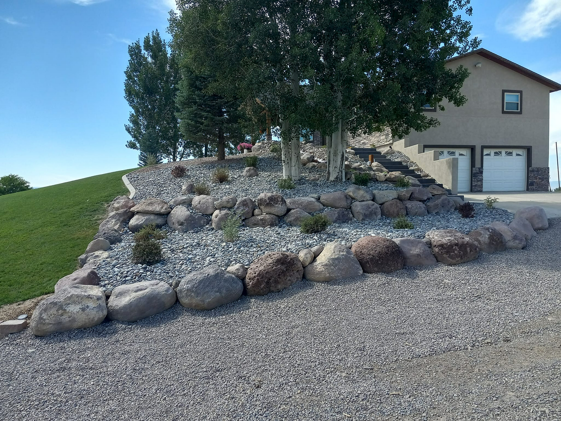 Backyard patio with stone paving and a retaining wall, adjacent to a house with a covered porch.