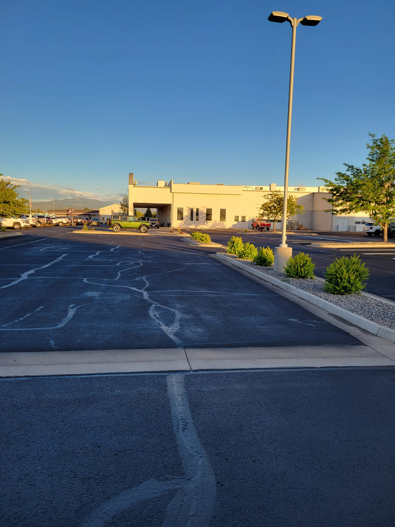 Empty asphalt parking lot, light pole, building in the background, blue sky.
