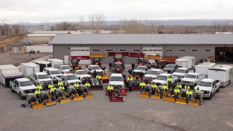Group of workers and snow removal vehicles outside a building.