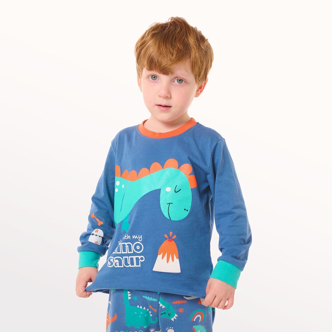 Niña modelando un pijama de dinosaurio azul sobre un fondo blanco.