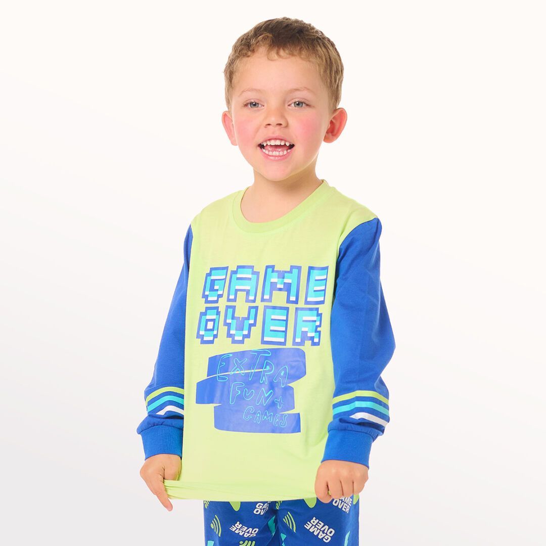 Niña posando con una rodilla levantada, vestida con pijama azul y calcetines sobre un fondo blanco de estudio.