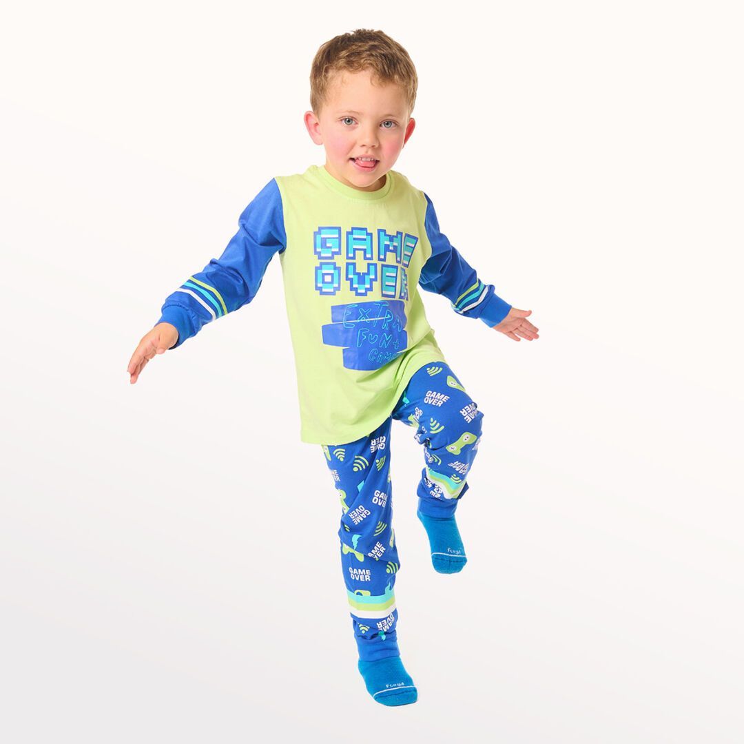 Niña posando con una rodilla levantada, vestida con pijama azul y calcetines sobre un fondo blanco de estudio.