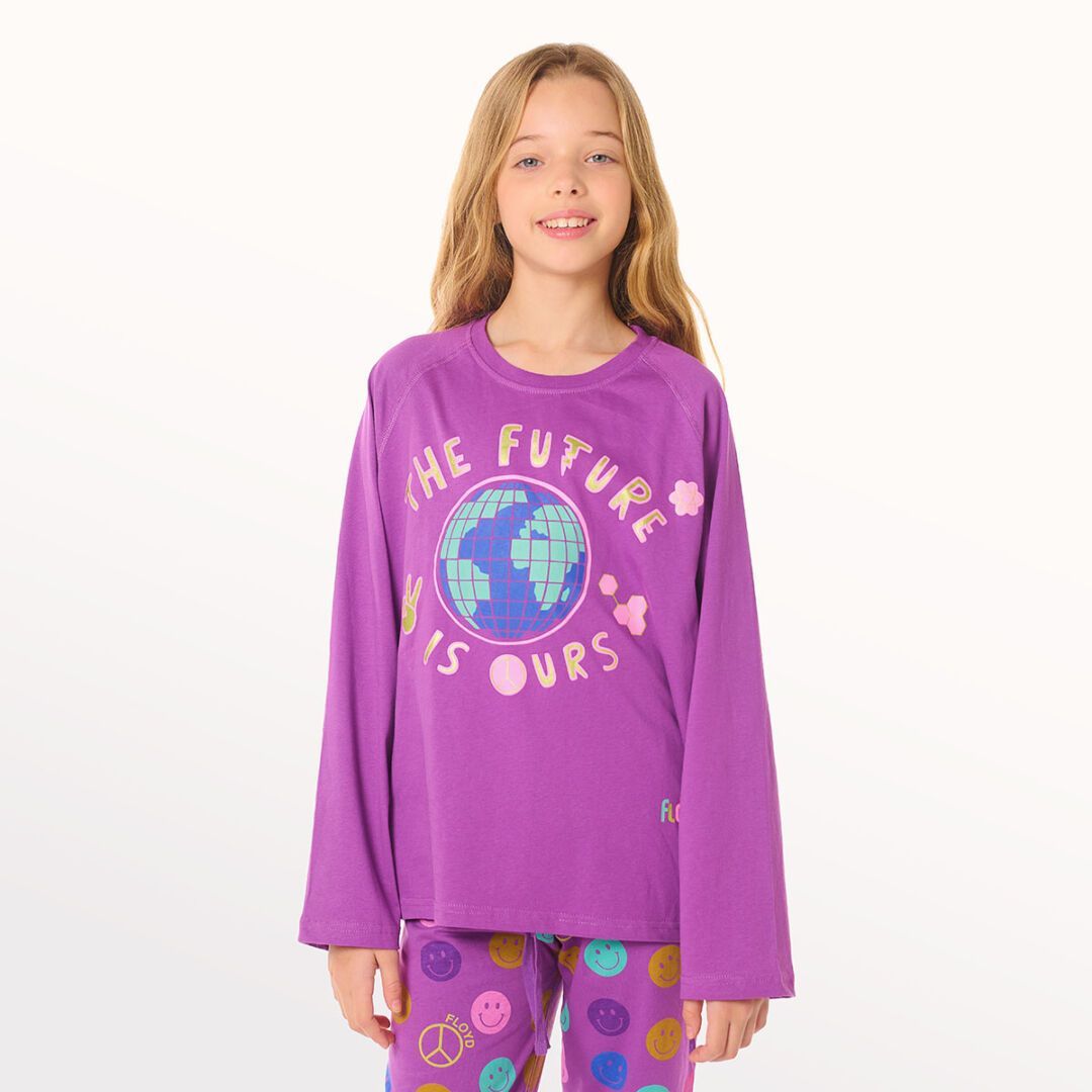 Niña con camiseta morada y pantalones estampados posando sobre un fondo blanco.