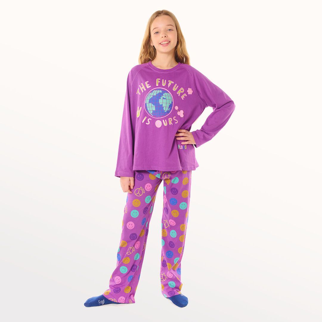 Niña con camiseta morada y pantalones estampados posando sobre un fondo blanco.