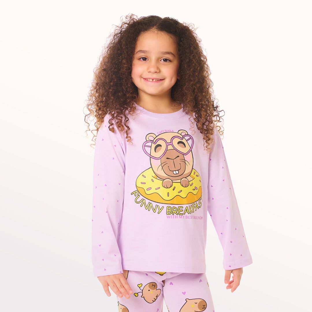 Niña con pijama de estampado de búho morado de pie sobre un fondo blanco.