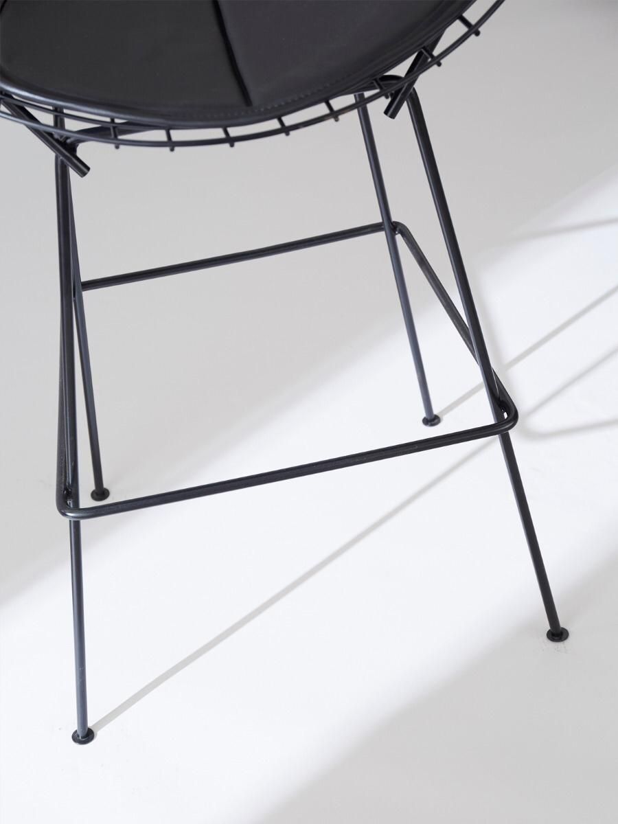 Taburete de bar negro con estructura de alambre, respaldo y asiento curvos sobre fondo blanco.