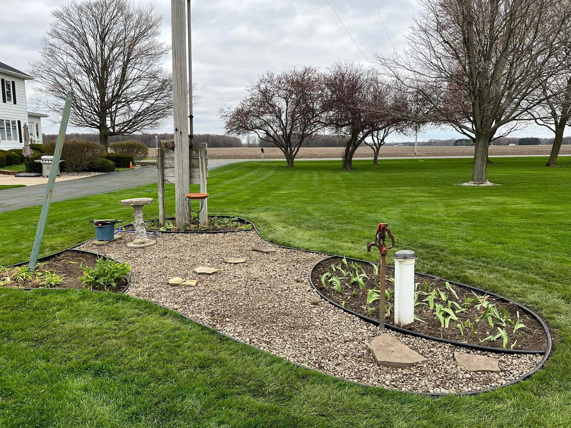 A yard with green grass, a flower bed with plants, and a flagpole on an overcast day.