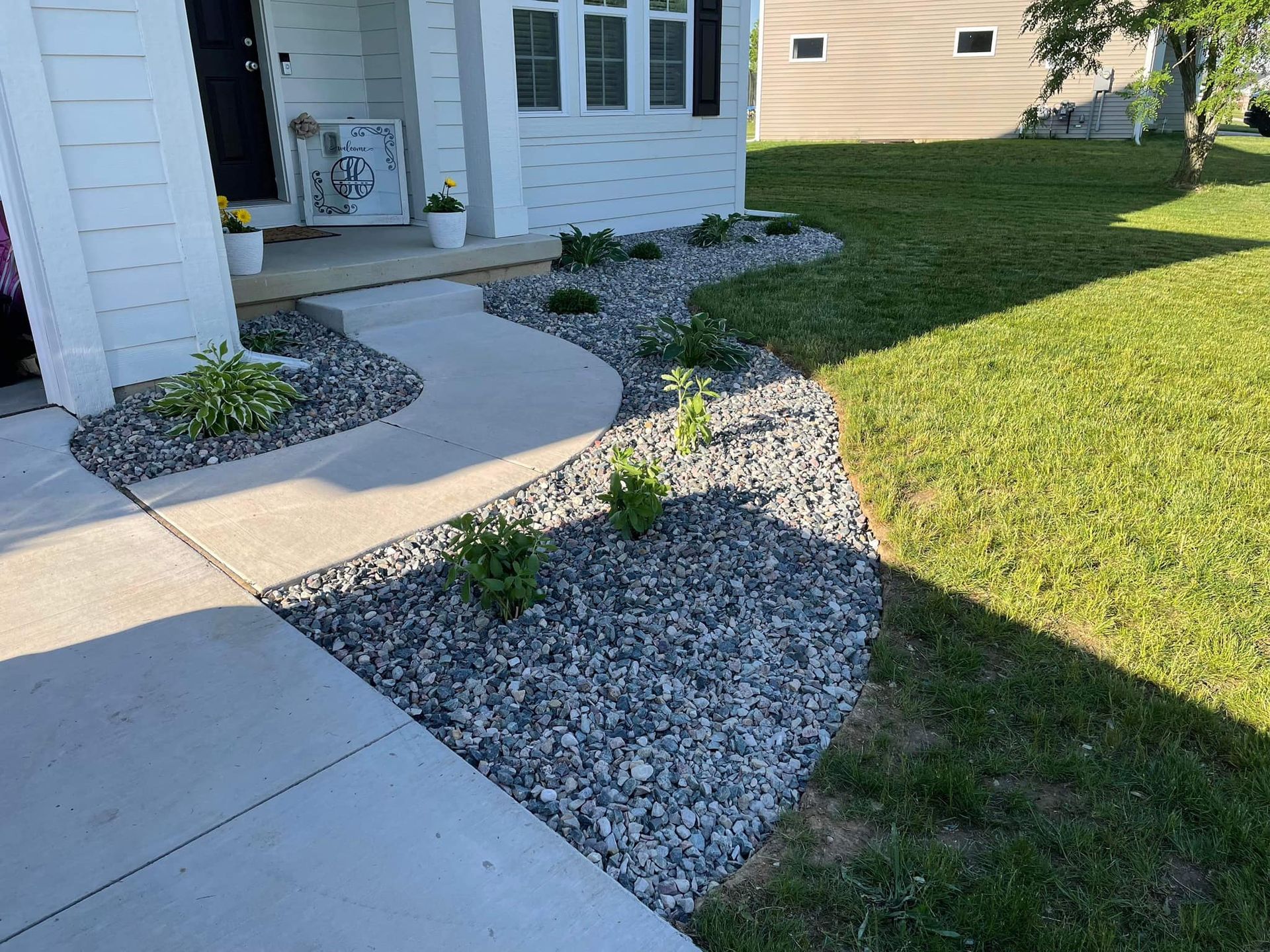 A house front with a concrete walkway, gravel landscaping, and green grass.