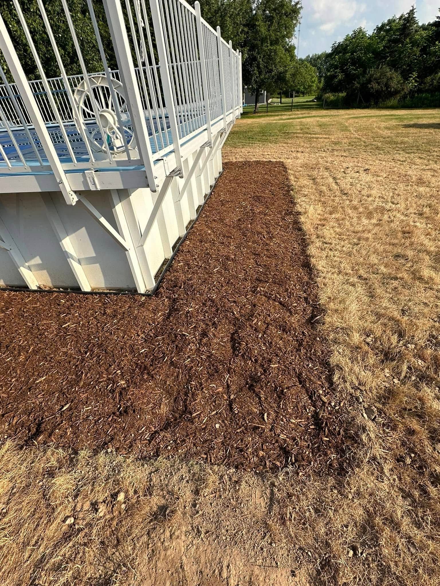 Brown mulch border next to a white deck, on dry grass.