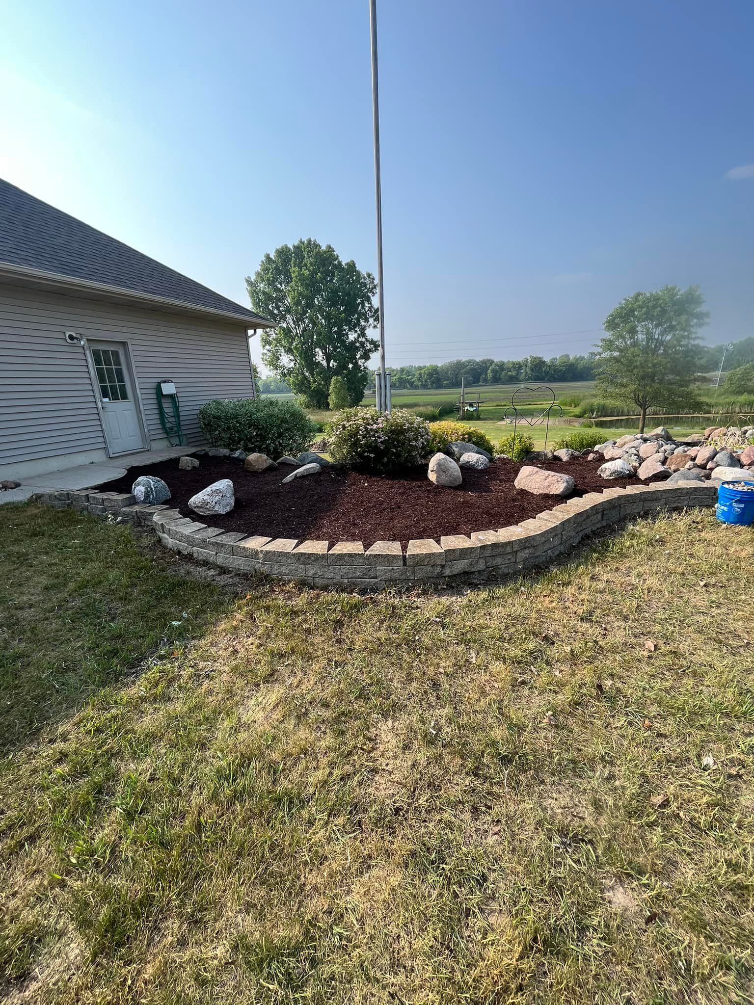 Landscaped flower bed with stone border, mulch, and large rocks in front of a house.