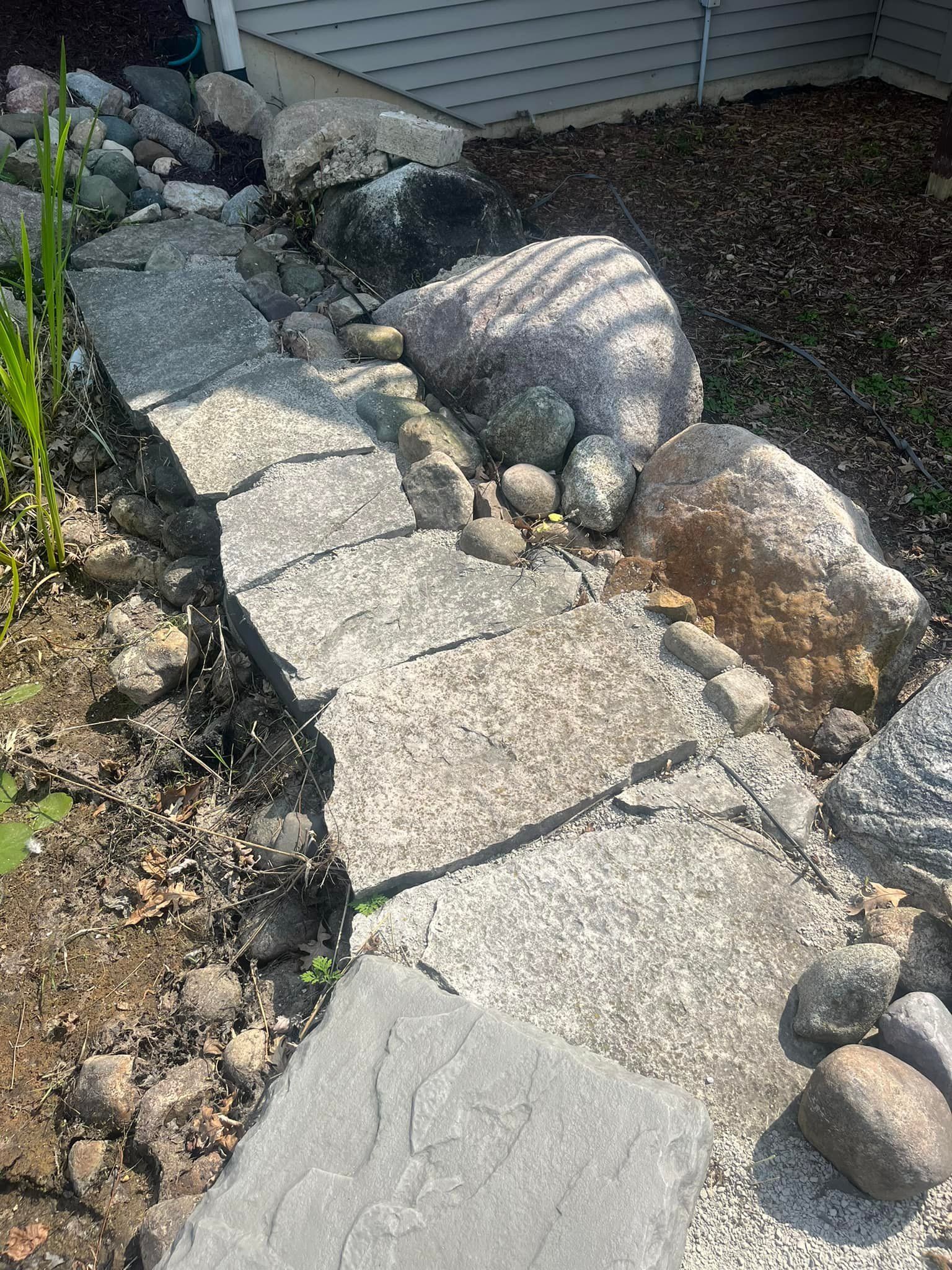 Stone pathway winding along a garden bed with large rocks and gravel.