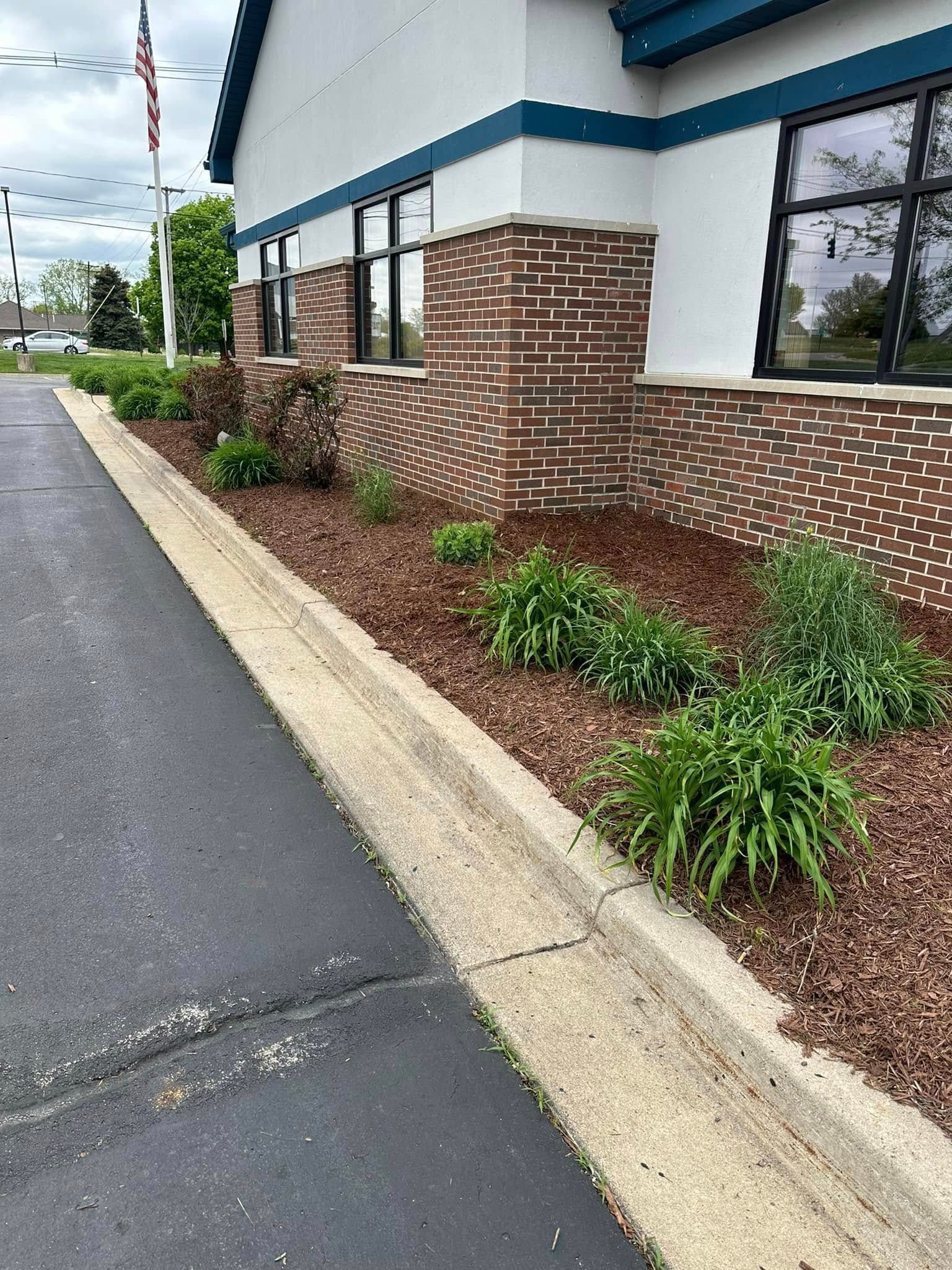 Sidewalk and curb with building, red brick, windows, and plants.