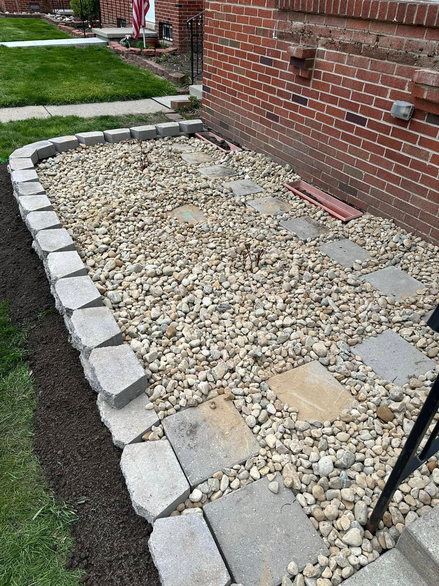 A rock garden bed with square stepping stones and a brick building to the right.