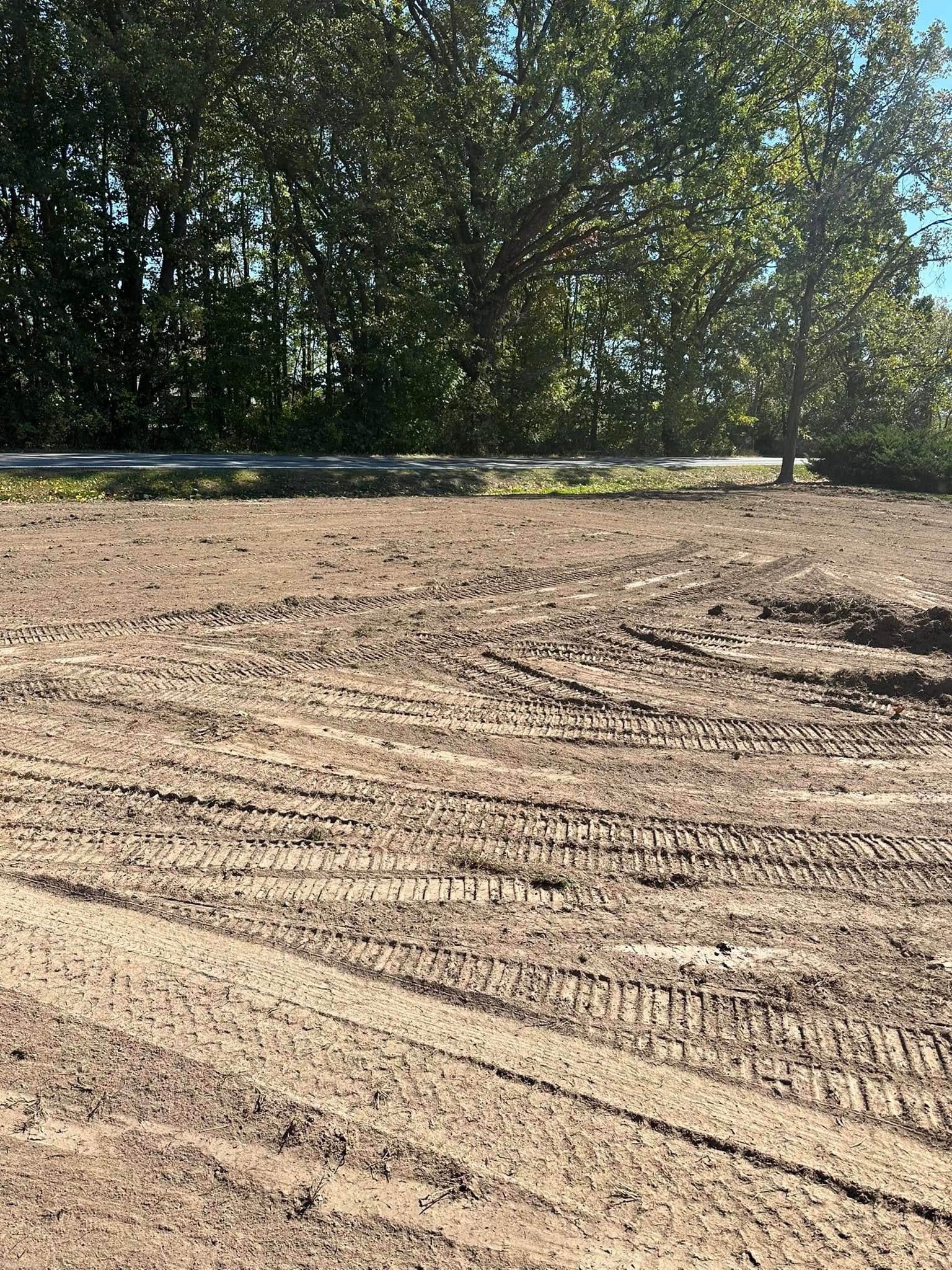 Dirt terrain with vehicle tire tracks, background of trees and a guardrail.