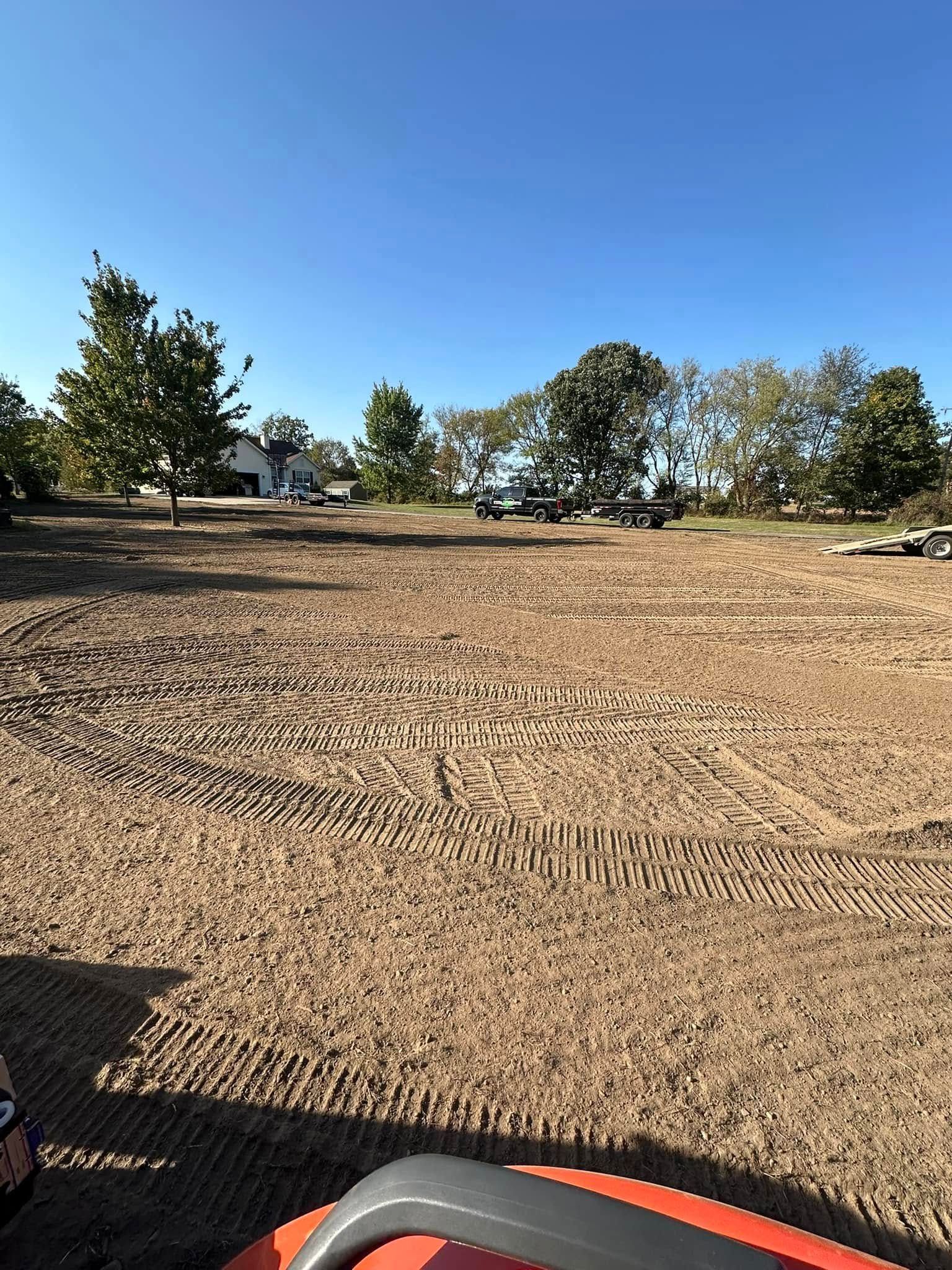 Dirt field with tire tracks, trees in the background, blue sky.