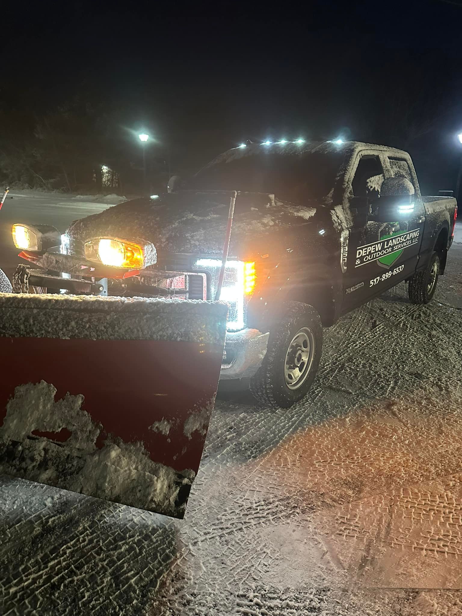 Snow plow truck plowing snow at night, headlights on.