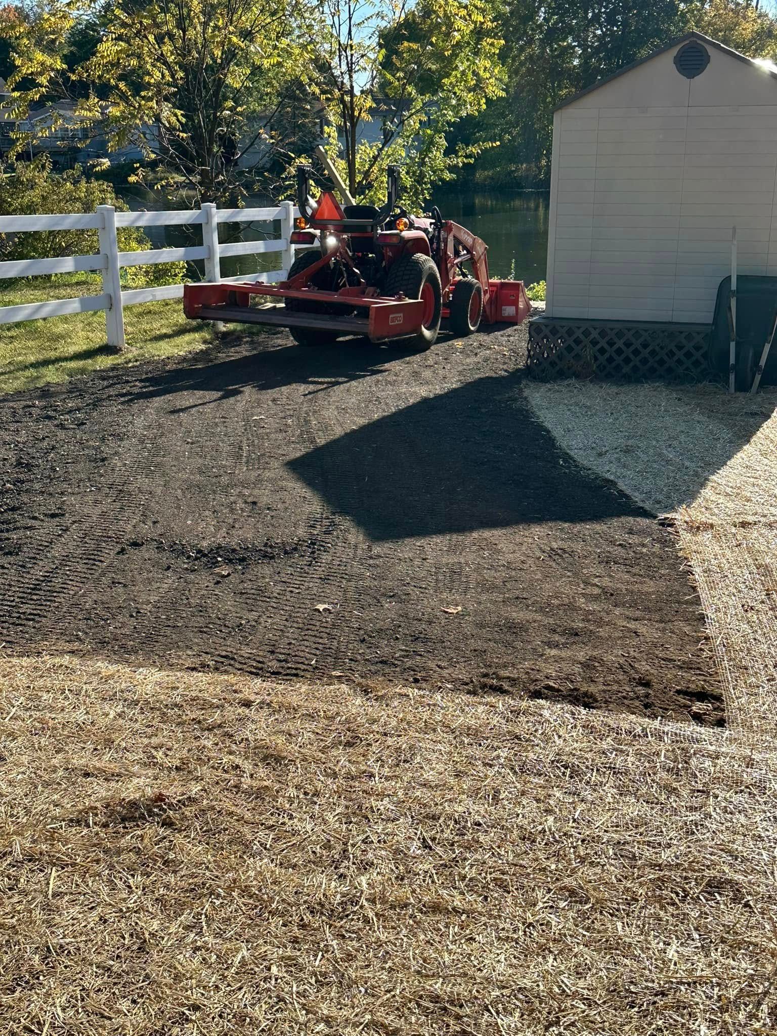 Tractor on prepared soil beside a white fence and a shed.