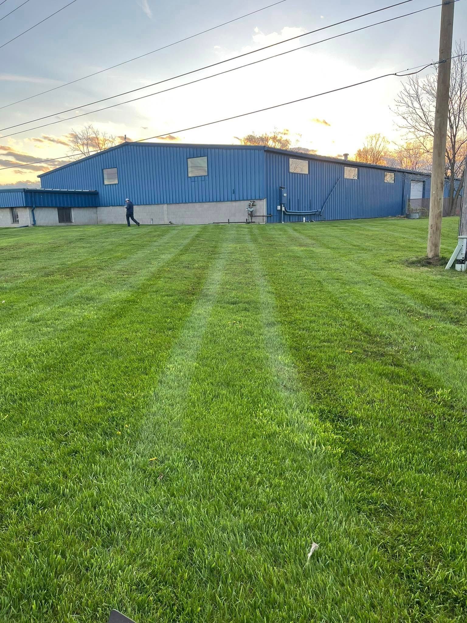 Large blue building with two people, mowed grass, power lines.