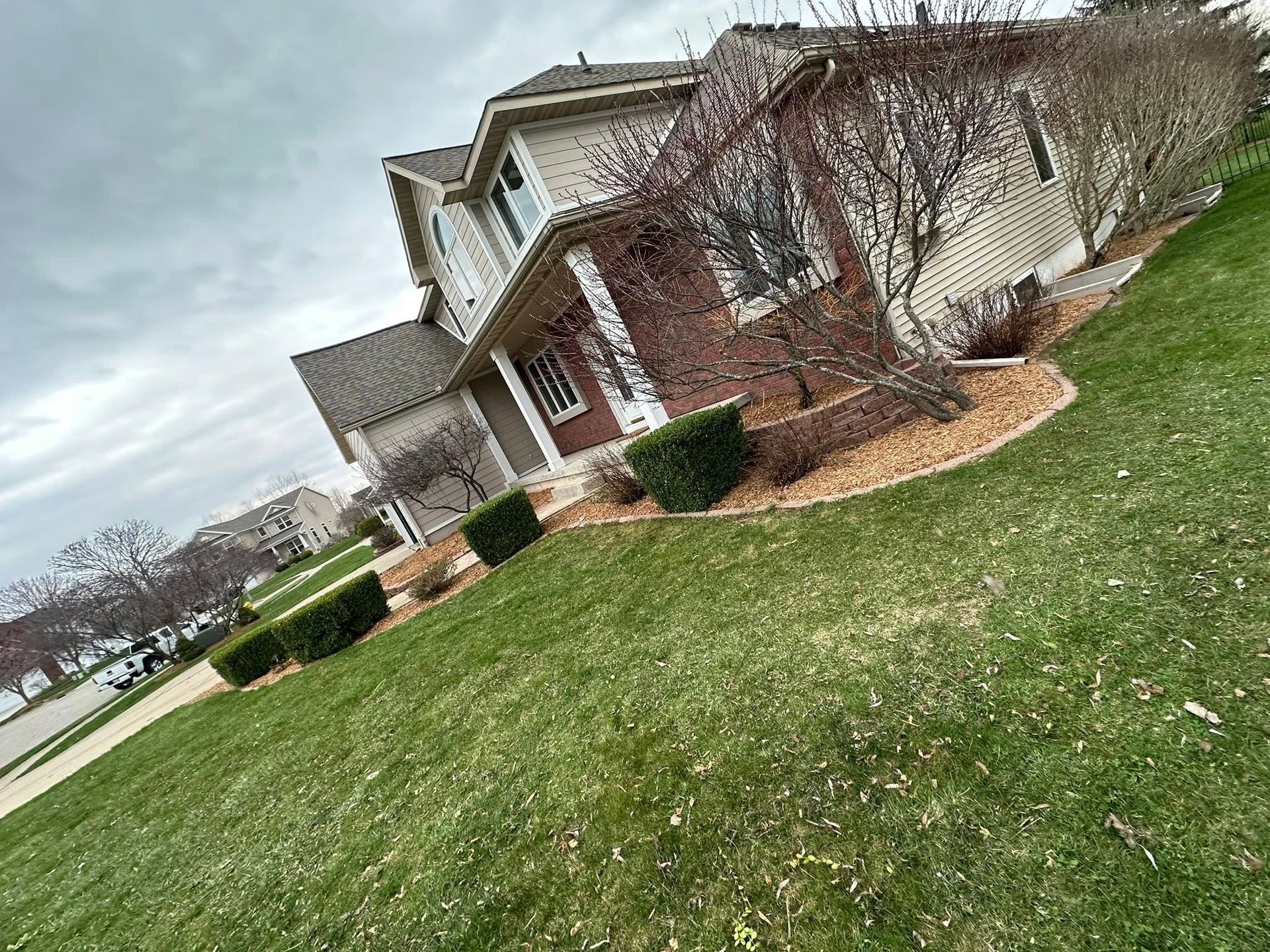 Two-story house with brick accents, surrounded by a green lawn and cloudy sky.