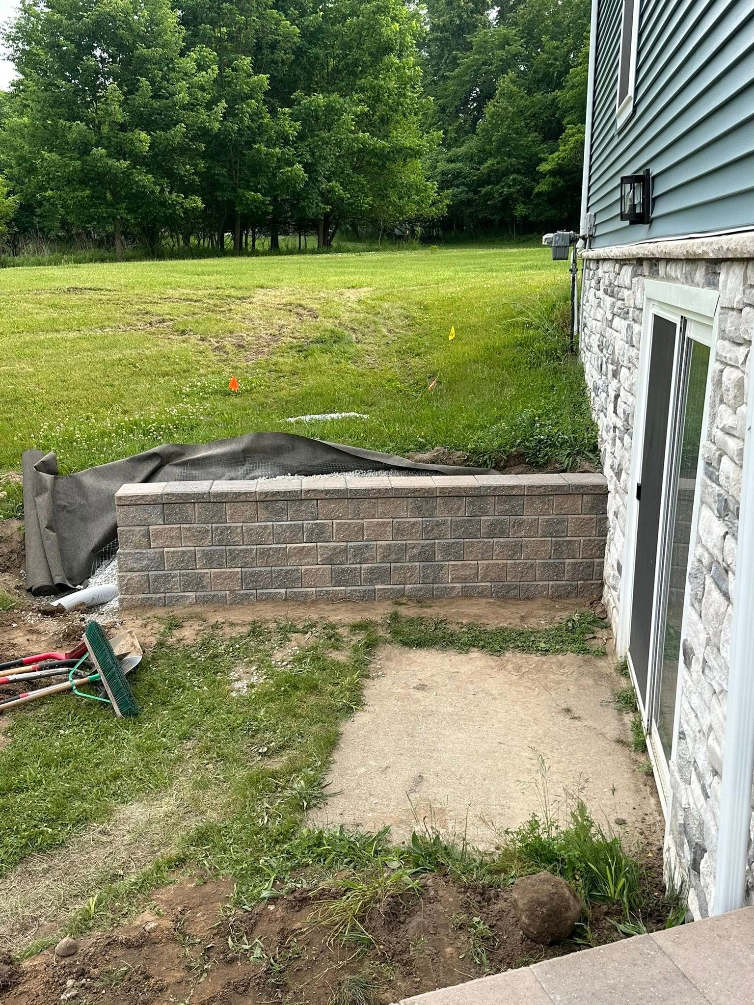 Brick retaining wall next to a house with a door, on a grassy slope. Construction materials are visible.