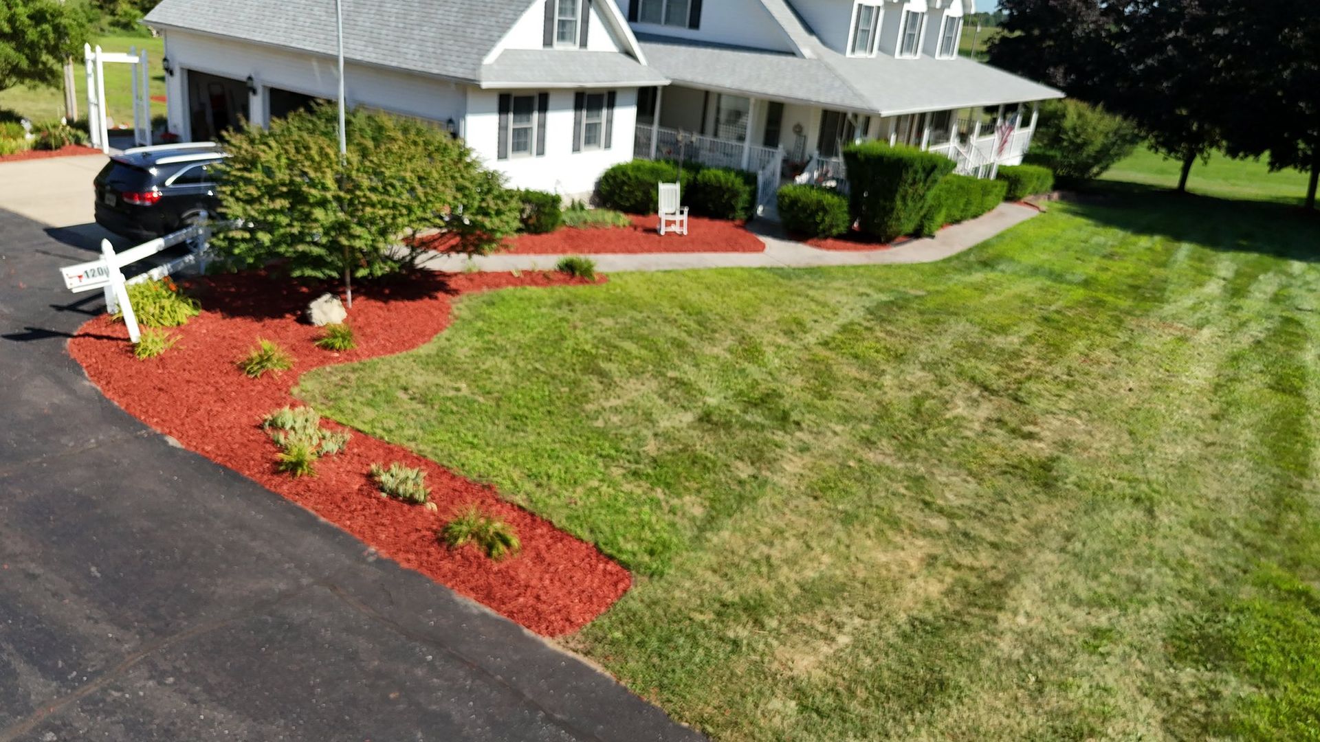 A house with a large green lawn, red mulch flowerbeds, and a black driveway.