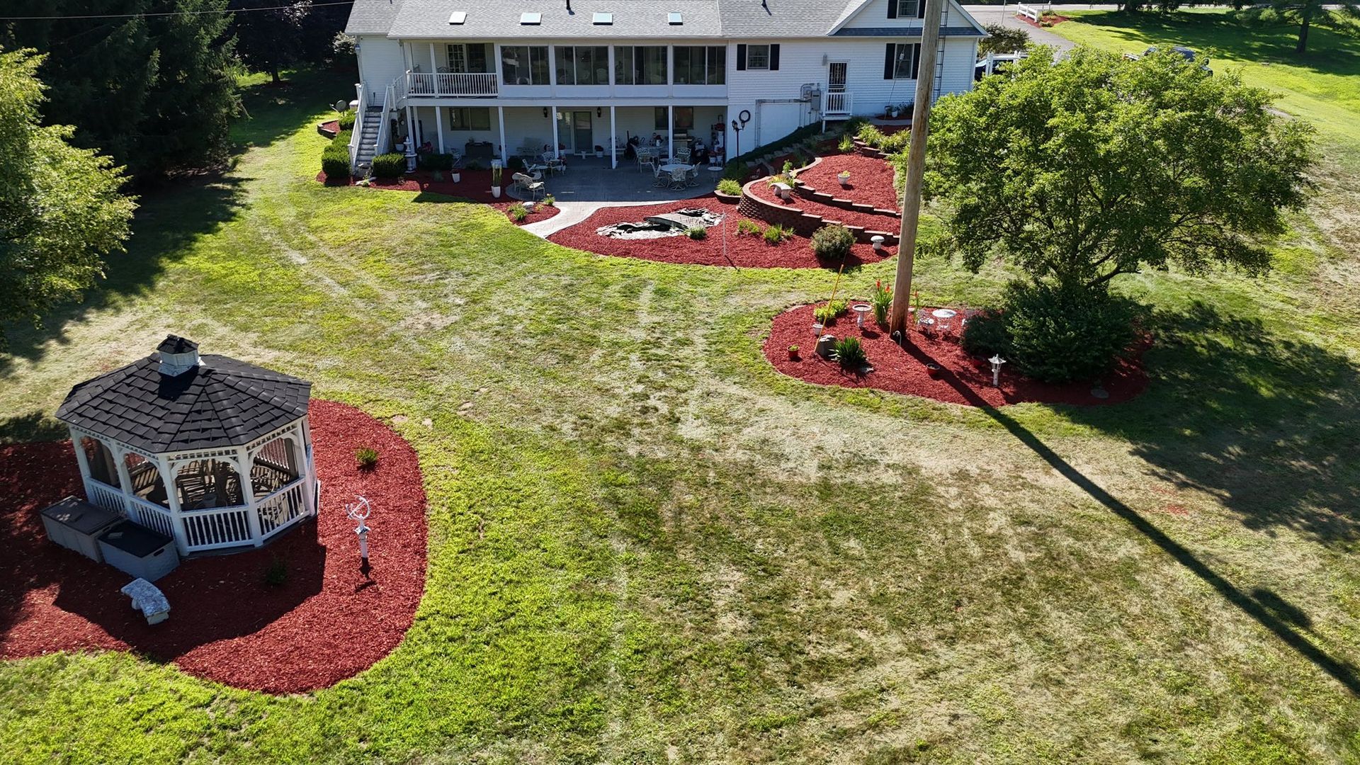 Aerial view of a white house with a gazebo, patio, and landscaped yard featuring red mulch beds.