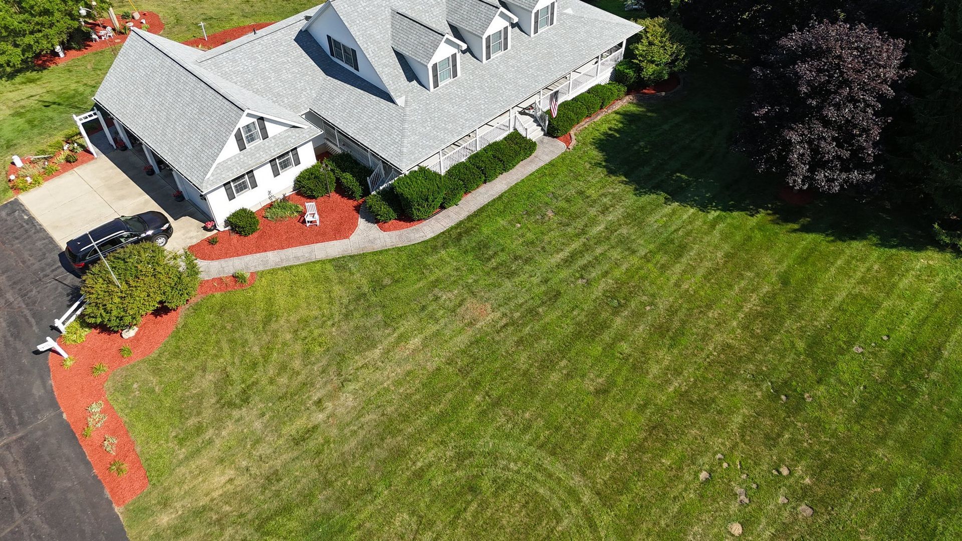 Aerial view of a gray-roofed house with a large green lawn and red mulch beds.