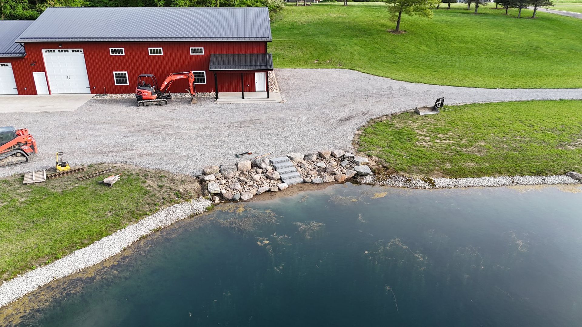 Red building with heavy machinery beside a pond; gravel path and stone steps.