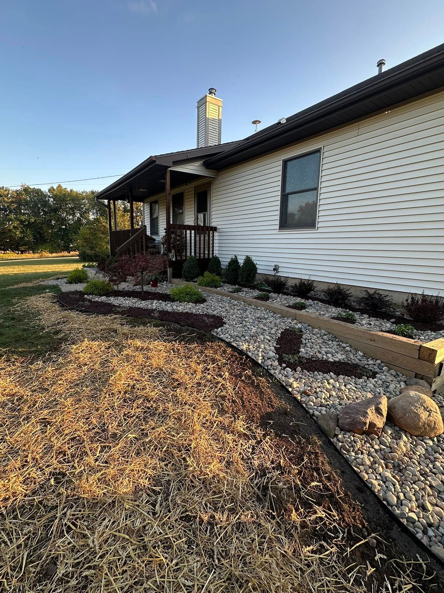 Exterior of a house with a porch and landscaped garden bed. Mulch and stones surround plants.