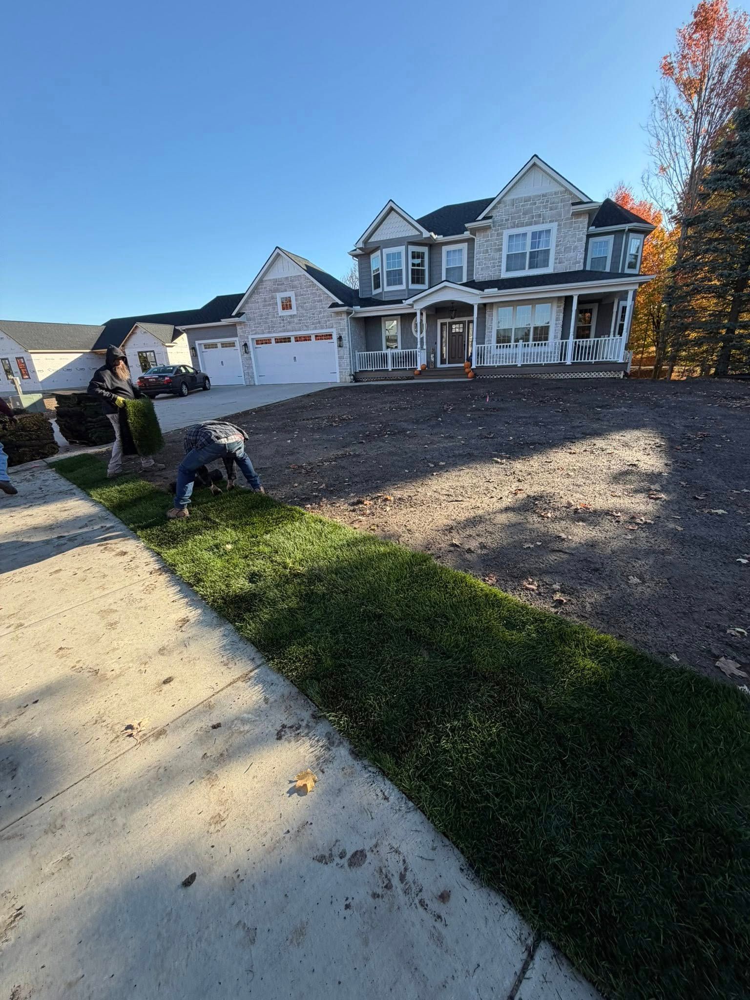 People working on lawn near a two-story house with gray siding under a blue sky.