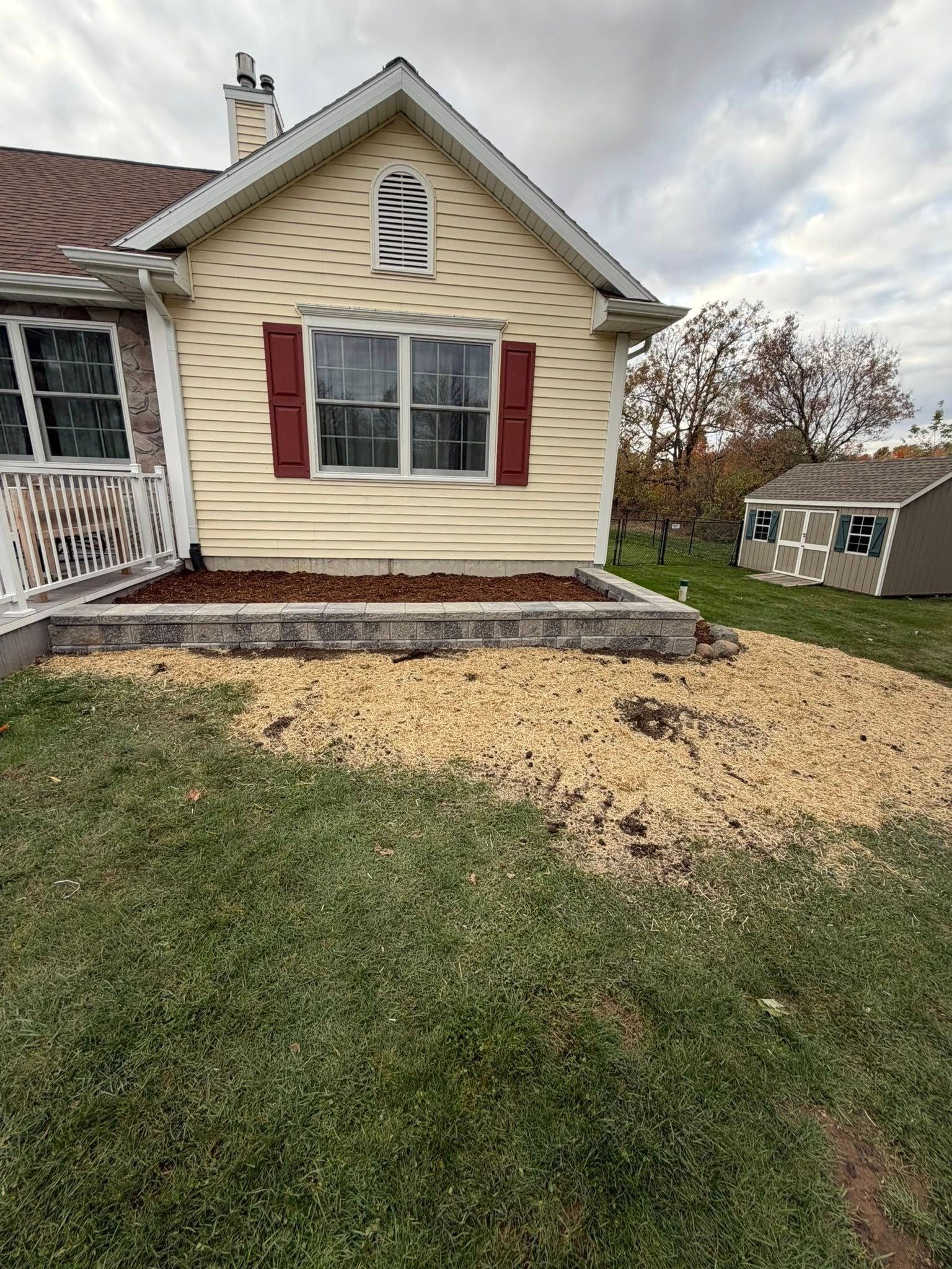Cottage with yellow siding, red shutters, and a rock-covered lawn against a cloudy sky.