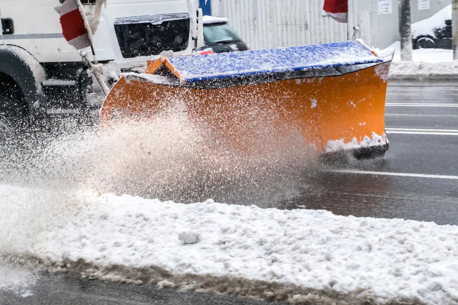 Snowplow clearing snow from a road; orange blade, blue cover, white truck.
