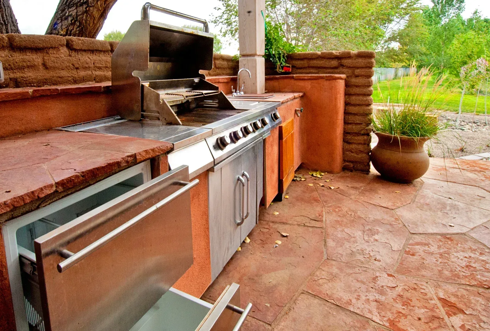 Outdoor kitchen with stainless steel grill, fridge, and red brick counters.