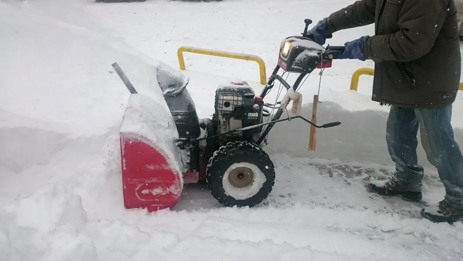 Person operating a red snowblower on a snow-covered sidewalk, clearing a path.