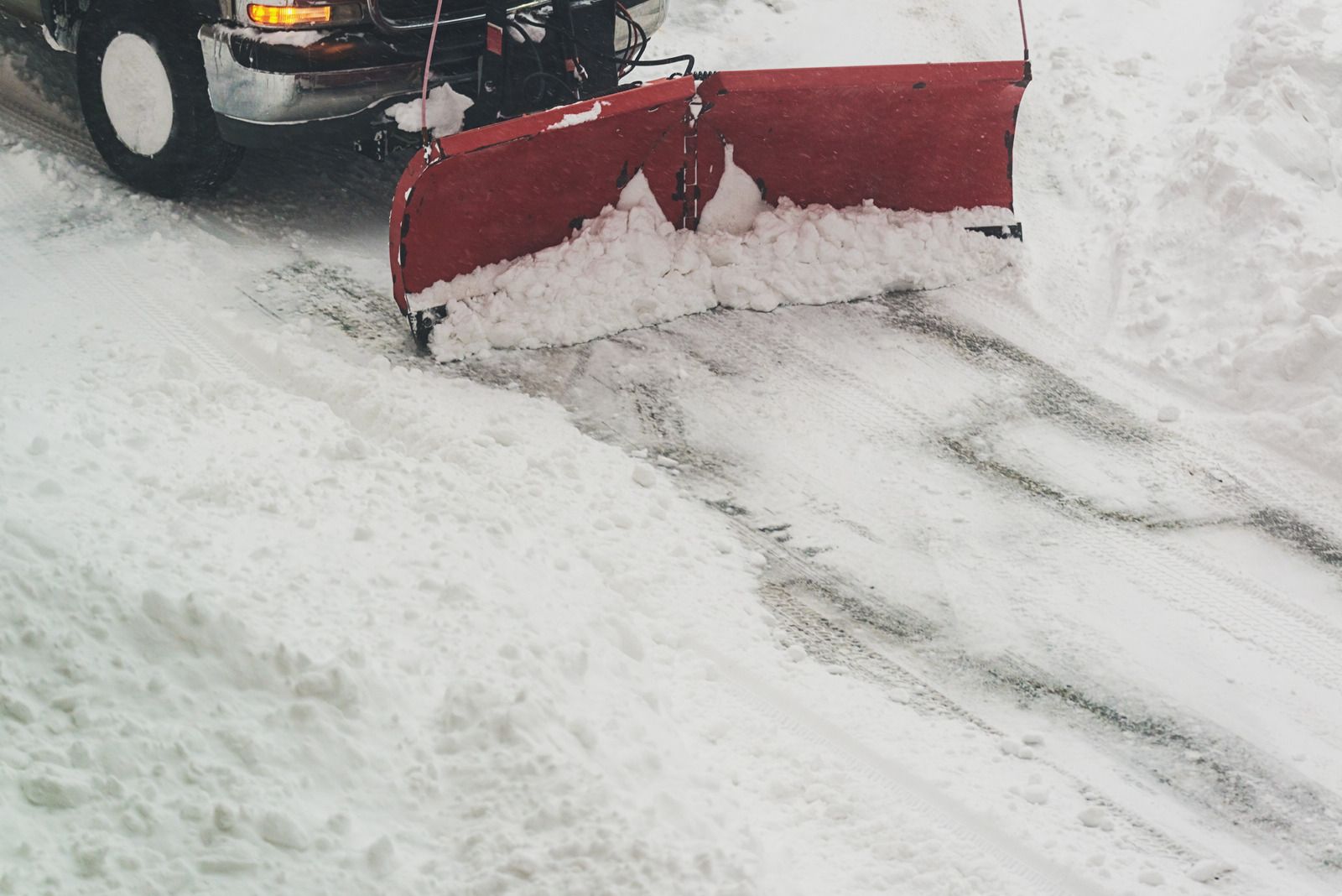 Snowplow clearing snow from a road; red blade pushing white snow to the side.