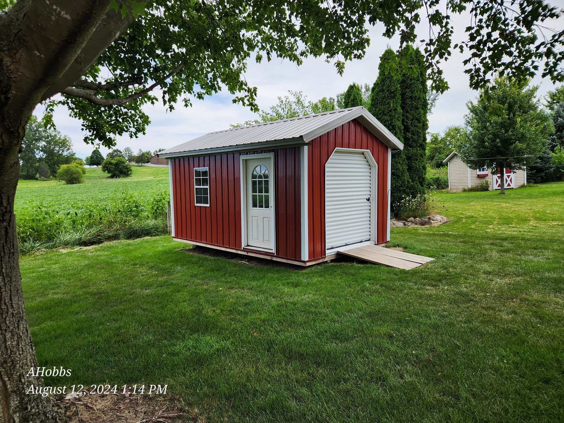A small red shed with a white garage door is in the middle of a grassy field.