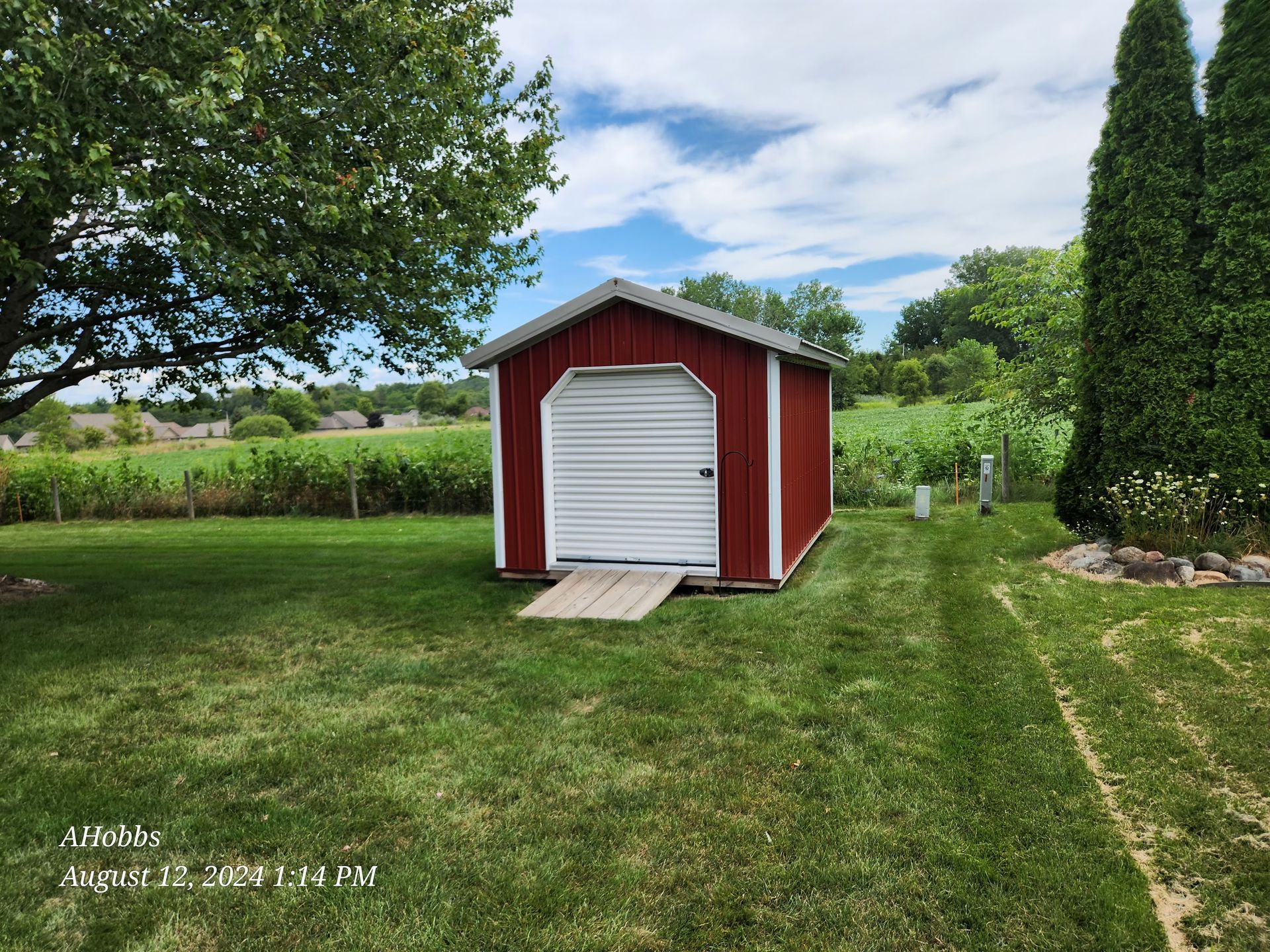 A red shed with a white door is sitting in the middle of a lush green field.