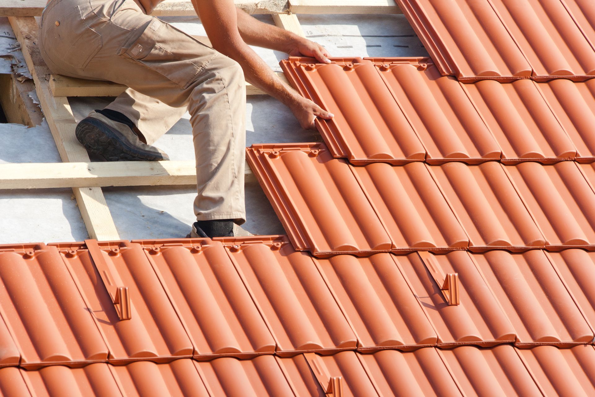 A worker carefully laying tiles on a roof, showcasing skilled craftsmanship in roofing installation.